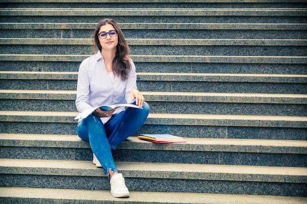 Una chica con gafas con un libro se sienta en los escalones