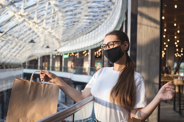 Chica con gafas y una máscara protectora en un centro comercial con compras