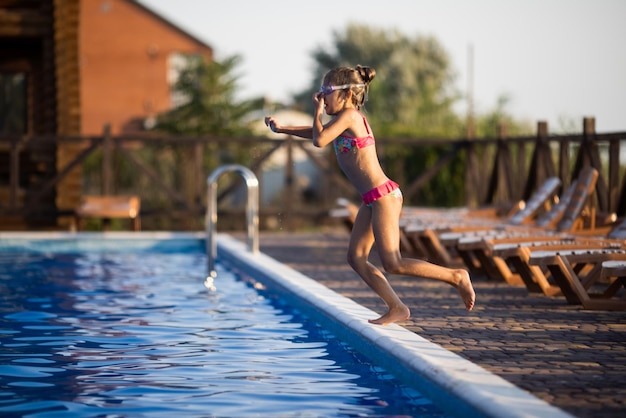 Una chica con gafas de natación salta a una piscina con agua clara en el fondo de una cálida puesta de sol de verano