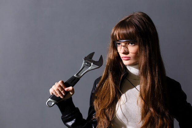 Chica con gafas protectoras con llave ajustable sobre un fondo oscuro