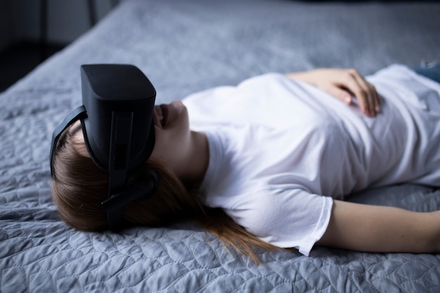 Chica con gafas de realidad virtual. Ella está tocando algo y expresa las emociones de esta experiencia en la cama.