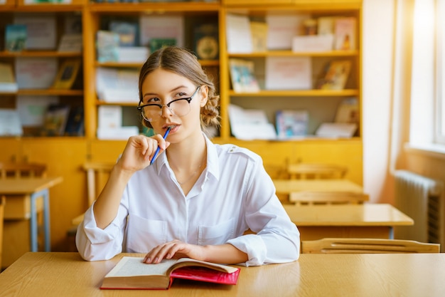 Chica con gafas sentado en una mesa con un libro en el aula