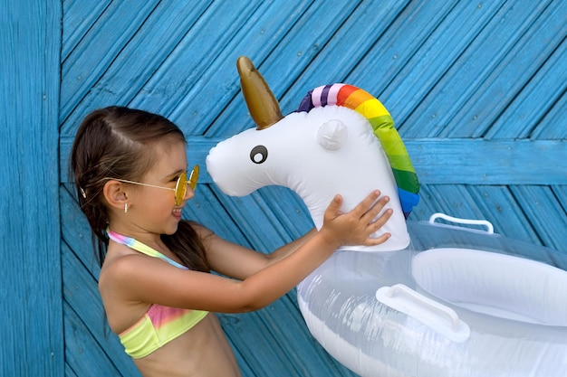 Chica con gafas de sol amarillas sostiene un círculo de natación en forma de unicornio