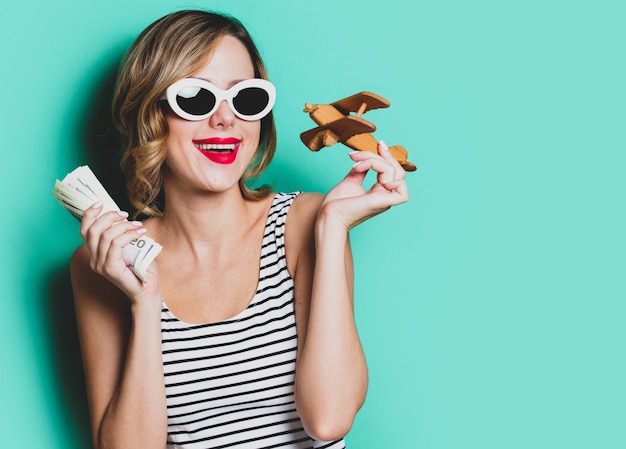 Chica en gafas de sol con dinero y aeroplano de madera.