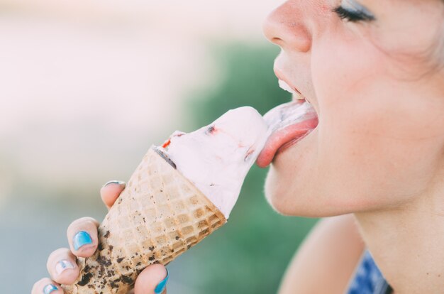 Chica con gafas de sol lame helado al aire libre, vestida con overoles de mezclilla