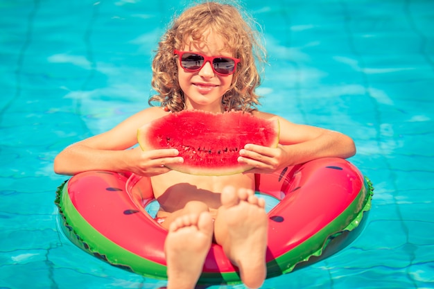 Chica con gafas de sol rojas sosteniendo una sandía en un inflable de sandía en la piscina