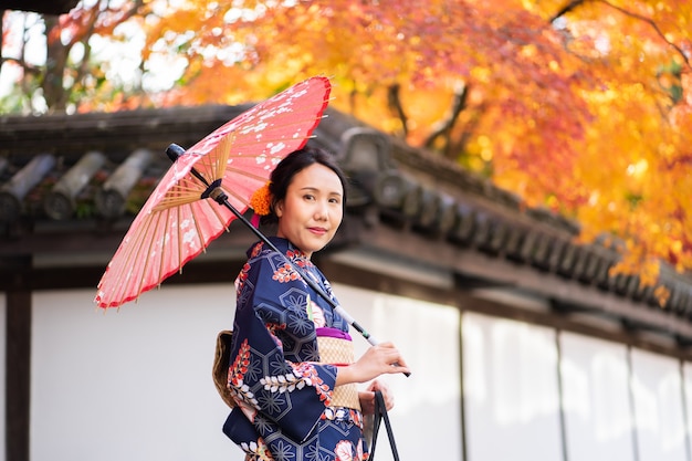 Chica Geishas con kimono japonés entre puerta de madera roja Tori