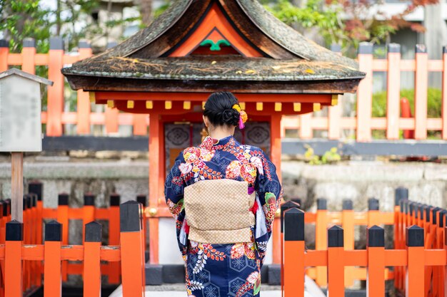 Foto chica geishas vistiendo kimono japonés entre la puerta de madera roja tori en el santuario fushimi inari en kioto,