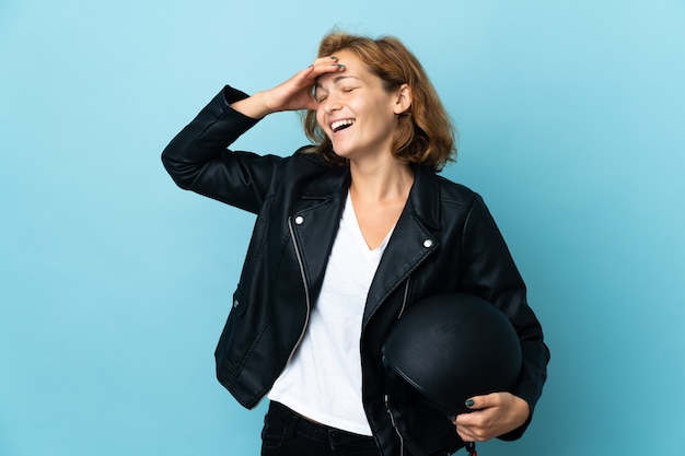 Chica georgiana sosteniendo un casco de motocicleta aislado en la pared azul sonriendo mucho