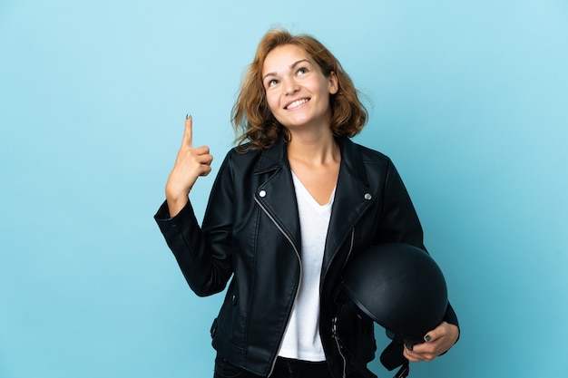 Chica georgiana sosteniendo un casco de motocicleta aislado sobre fondo azul apuntando hacia una gran idea