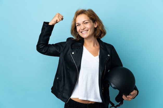 Chica georgiana sosteniendo un casco de motocicleta aislado sobre fondo azul haciendo un gesto fuerte