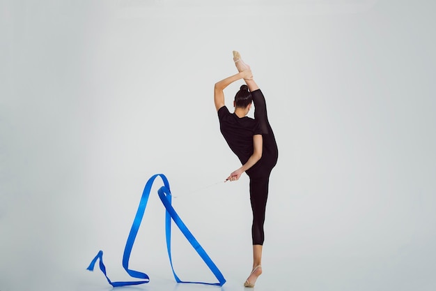 Chica de gimnasia rítmica en un mono de pie muestra un ejercicio con una cinta en divisiones verticales