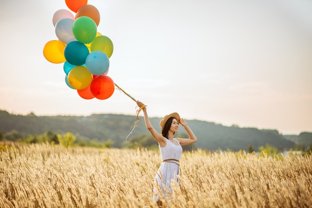 Chica con globos de colores en un campo de centeno. Mujer bonita en prado de verano