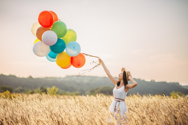 Chica con globos de colores en un campo de centeno