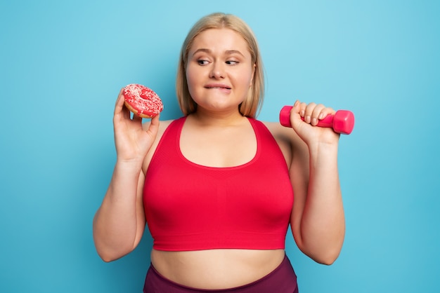 Chica gorda piensa comer rosquillas en lugar de hacer gimnasia. Concepto de indecisión y duda.