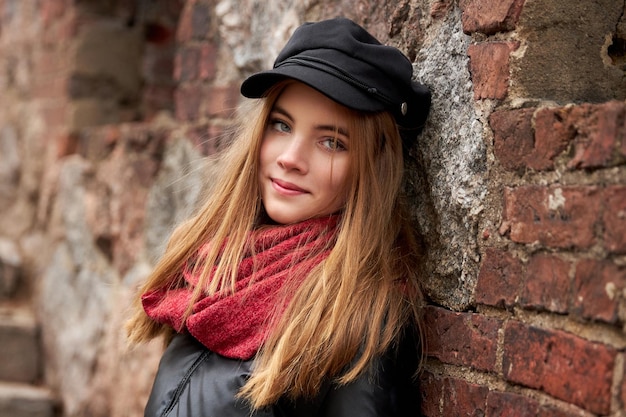 Chica con una gorra negra y una bufanda roja contra una pared de ladrillos