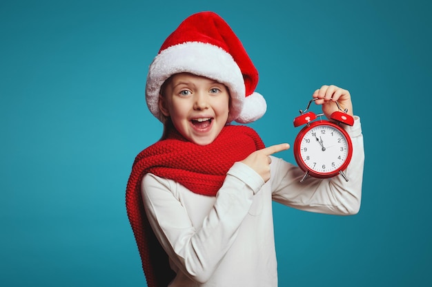 Chica con gorro de Papá Noel y mostrando la hora en el despertador rojo en