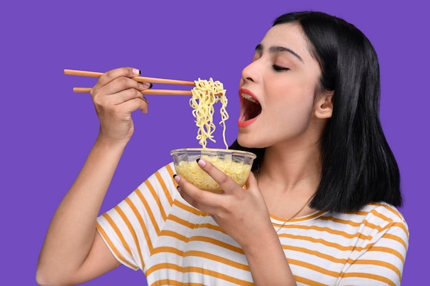 Chica gourmet comiendo fideos sobre fondo morado modelo paquistaní indio