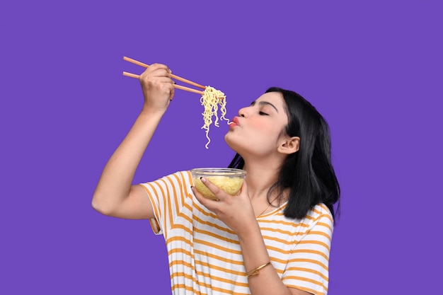 Chica gourmet comiendo fideos sobre fondo morado modelo paquistaní indio