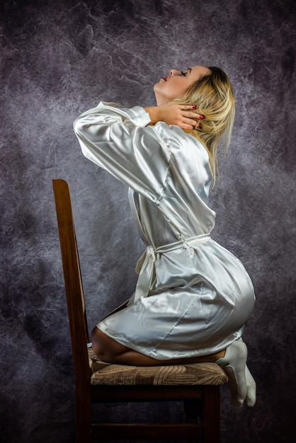 Chica con gran cabello y maquillaje en túnica erótica blanca y ropa interior en estudio