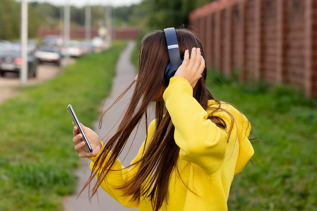 Chica en grandes auriculares inalámbricos al aire libre en la calle escuchando música, sonriendo