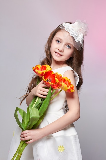 Chica con grandes ojos azules de anime y un ramo de flores de tulipán en sus manos. Día mundial de la madre, día de primavera, ramo de primavera en manos del niño. Cabello rubio largo y rizado