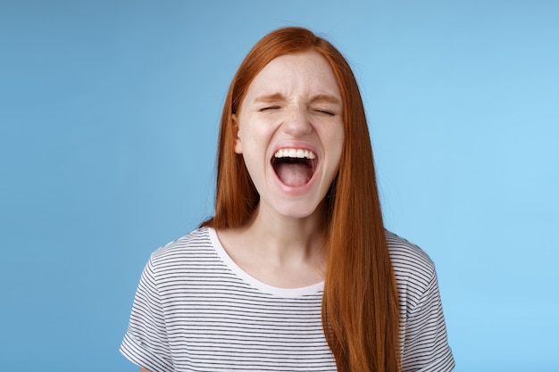 Chica gritando en voz alta mostrando actitud sacar el estrés de estar harto de quejarse de vida hursh gritando ojos cerrados gritando de pie enojado molesto fondo azul angustiado. Copia espacio