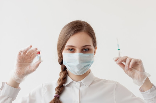 Chica con una guadaña en una máscara médica y guantes sostiene una botella de vacuna y jeringas.