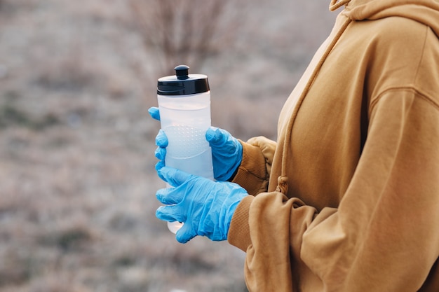 Chica con guantes azules sosteniendo una botella de agua en un trote durante el coronavirus