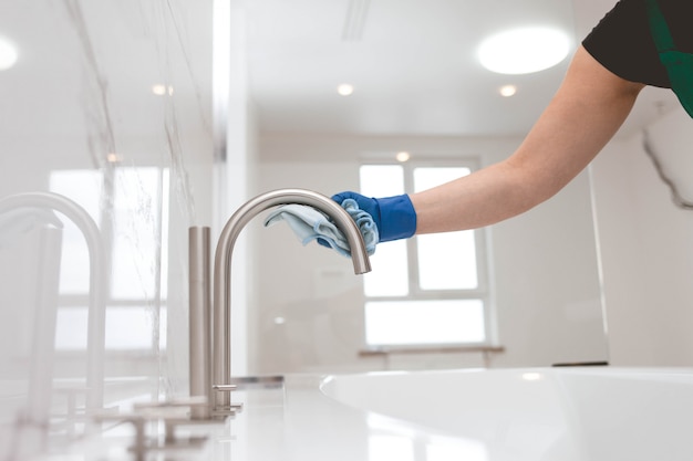 Chica en guantes limpia el grifo. Limpieza de baño