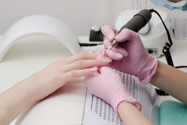 Chica en guantes maneja las uñas con una fresa para manicura