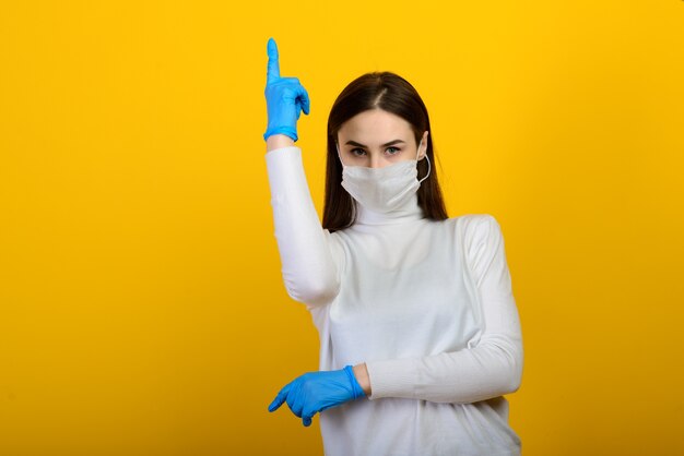 Chica en guantes médicos viste una máscara médica en su rostro sobre un fondo. Enfermedad respiratoria. COVID-19