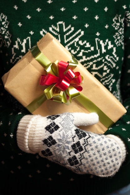 Chica en guantes y un suéter con un adorno de invierno tiene regalos de Navidad