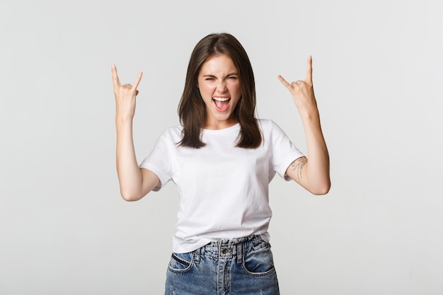 Chica guapa alegre que muestra un gesto de rock-on y disfruta de un concierto.