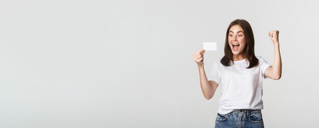 Foto chica guapa alegre regocijándose y mirando la bomba de puño de la tarjeta de crédito mientras triunfa backgr blanco