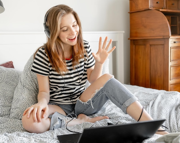 Chica guapa con auriculares y portátil en la cama