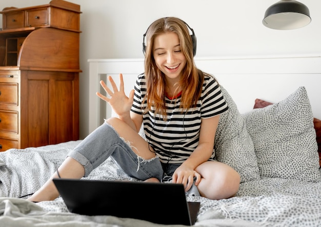 Chica guapa con auriculares y portátil en la cama