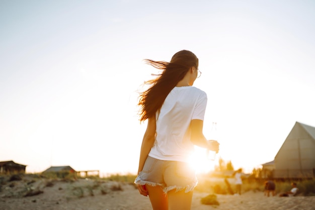 Chica guapa bebiendo cerveza en la playa al atardecer Mujer joven disfrutando de vacaciones en la playa Verano