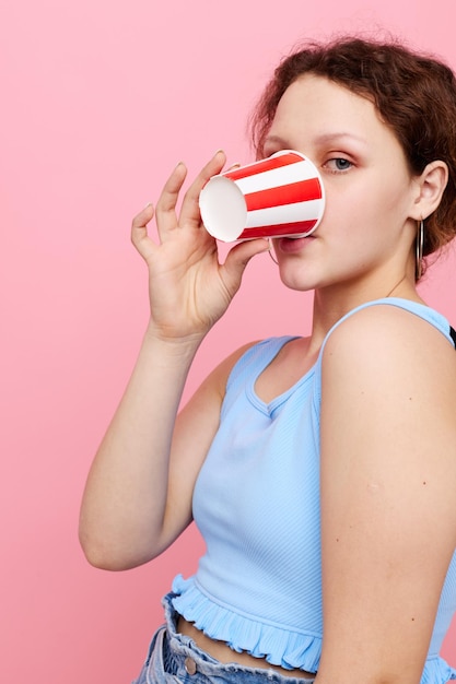 Chica guapa bebiendo de un vaso de bebida de fondo rosa primer plano inalterado