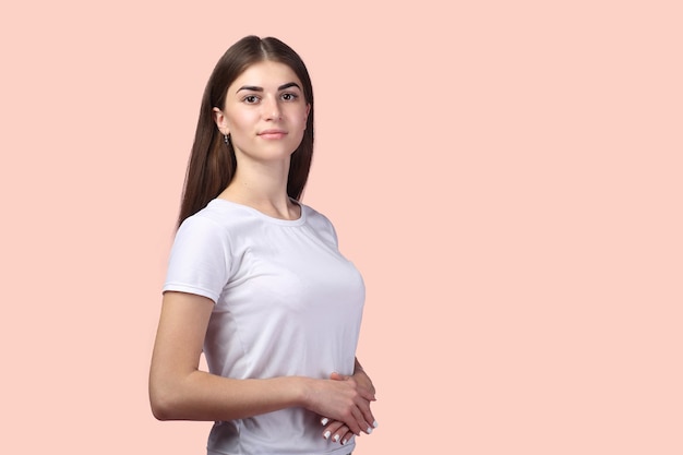 Chica guapa con cabello largo con camiseta blanca y posando sobre fondo rosa claro. Adorable morena de aspecto exitoso y profesional, con actitud positiva ante la vida.