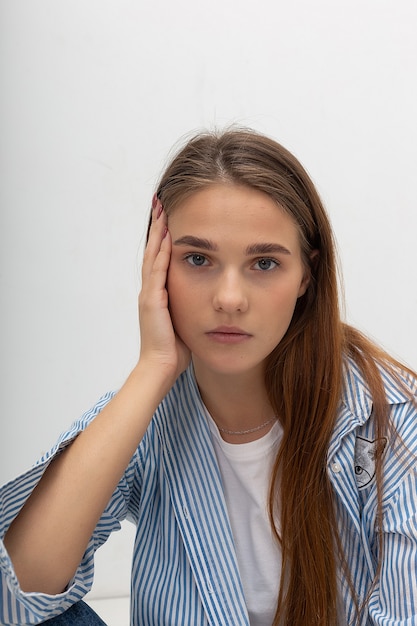 Chica guapa caucásica joven con el pelo largo en camisa a rayas azul se sienta en el estudio