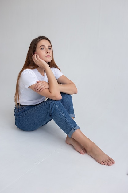 Chica guapa caucásica joven con el pelo largo en camiseta, pantalones vaqueros azules en el estudio