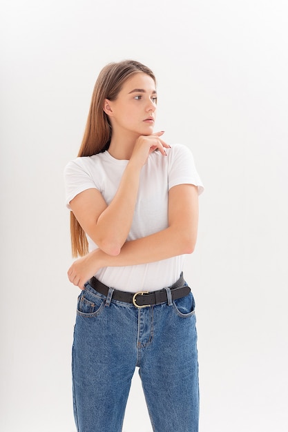 Chica guapa caucásica joven con el pelo largo en camiseta, pantalones vaqueros azules en el estudio