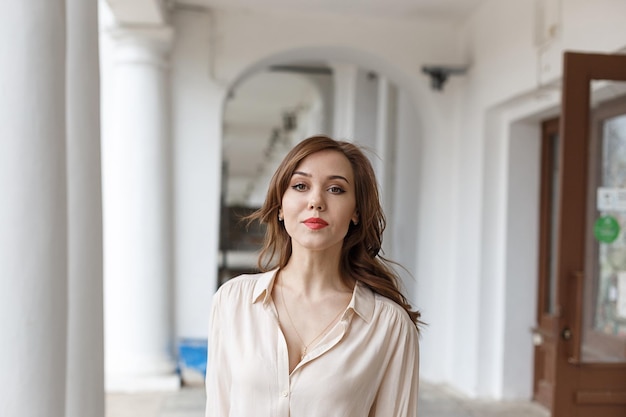 Chica guapa caucásica con labios rojos cabello rizado en elegante blusa beige al aire libre