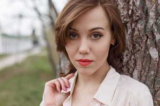 Chica guapa caucásica con labios rojos, pelo rizado en elegante blusa beige al aire libre