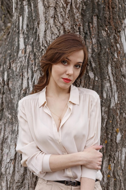 Chica guapa caucásica con el pelo rizado de labios rojos en elegante blusa beige al aire libre