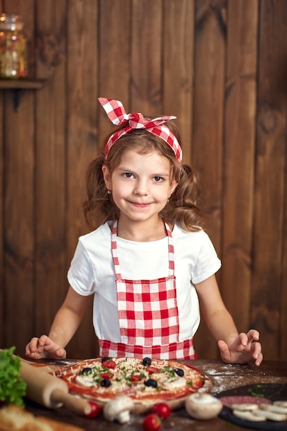 Chica guapa en delantal a cuadros cocinando pizza