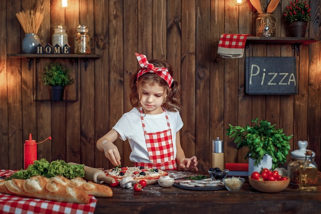 Chica guapa en delantal a cuadros rocía pizza con pizza verde