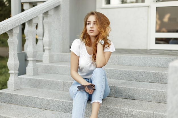 Chica guapa elegante sentada en los escalones cerca de la casa.