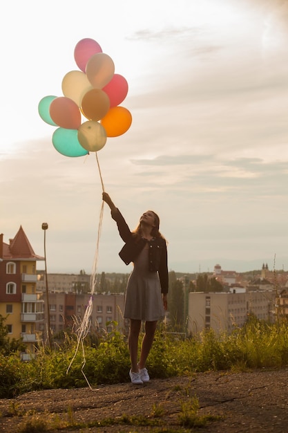 Foto chica guapa con grandes globos de colores caminando por las colinas cerca de la ciudad. centrarse en globos